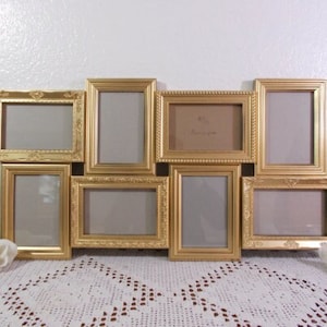 May include: A gold picture frame collage with nine openings. The frames are ornate and have a raised design. The frames are arranged in a staggered pattern.