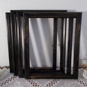 May include: Four black picture frames with a distressed finish. The frames are rectangular with a series of vertical bars within the frame. The frames are arranged in a slightly overlapping manner, showcasing their design and texture.