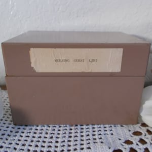 May include: A brown box with a white label that says "Meeting Guest List".