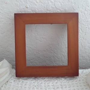 May include: Square wooden picture frame with a warm brown finish. The frame has a simple, classic design and is suitable for displaying photos or artwork. The frame is approximately 6 inches square.