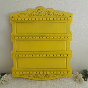 May include: A yellow wooden wall-mounted utensil holder with three shelves and a decorative floral design.