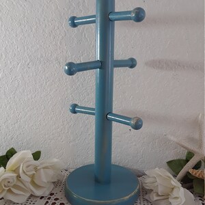 May include: A blue wooden towel rack with six arms for hanging towels. The rack has a distressed finish and a round base.