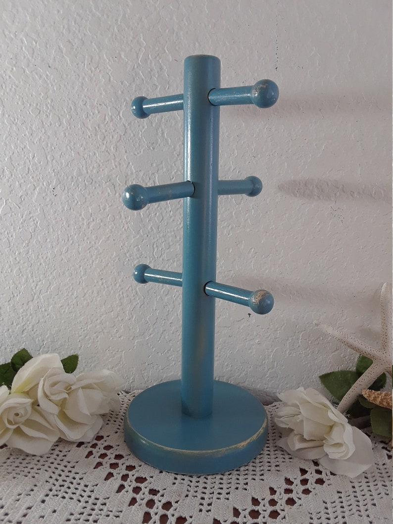 May include: A blue wooden towel rack with six arms for hanging towels. The rack has a distressed finish and a round base.