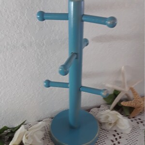 May include: A blue wooden mug tree with five hooks for hanging mugs. The tree has a round base and is painted a light blue color.