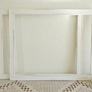 May include: Two white picture frames with ornate detailing. The frames are nested together, with the larger frame in front of the smaller frame.