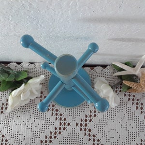 May include: A blue wooden stand with five arms for holding jewelry or other small items. The stand is on a white crocheted doily.