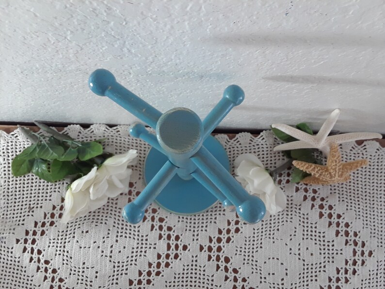 May include: A blue wooden stand with five arms for holding jewelry or other small items. The stand is on a white crocheted doily.