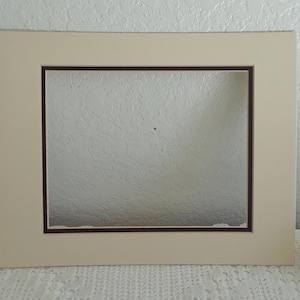 May include: A cream-colored picture frame with a brown mat and a rectangular opening. The frame is on a white surface.