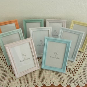 May include: A set of ten pastel-colored picture frames with a white mat and the text "Elegant Simple" printed on each. The frames are arranged on a white crocheted doily.