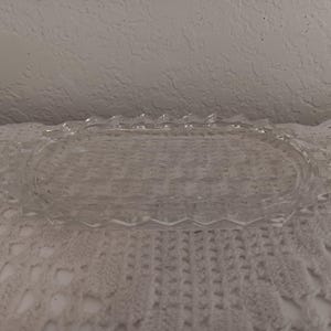 May include: A clear, oval-shaped glass serving tray with a decorative, scalloped edge. The tray has a textured, geometric pattern on the base and is ideal for serving appetizers or displaying small items. The tray is approximately 10 inches long.