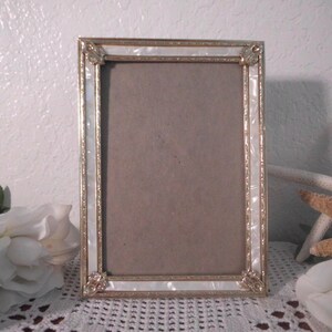 May include: A white and gold picture frame with a decorative design. The frame has a white pearl-like finish with gold accents.