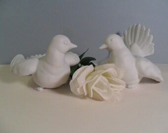 May include: Two white ceramic doves facing each other with a white rose in between them.