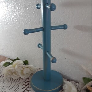 May include: A blue wooden mug rack with five hooks. The rack has a round base and is painted a light blue color.