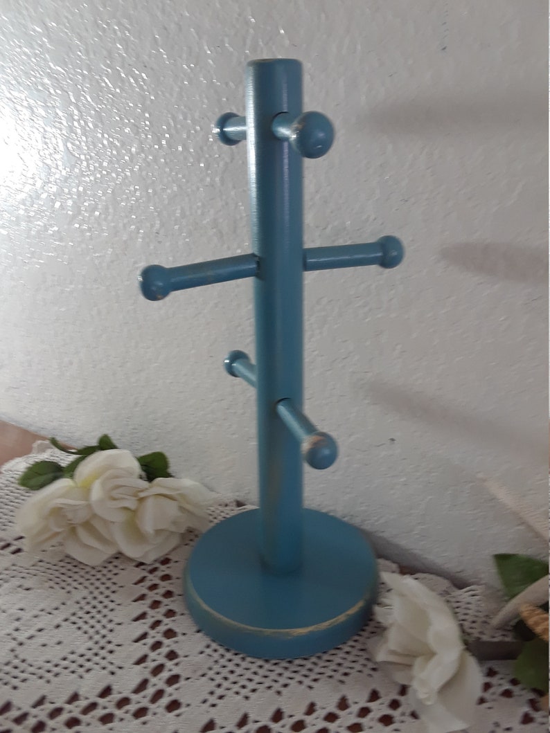 May include: A blue wooden mug rack with five hooks. The rack has a round base and is painted a light blue color.