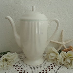 May include: White ceramic coffee pot with a green trim around the lid and a ribbed design. The pot is sitting on a white crocheted doily with white roses and a starfish.