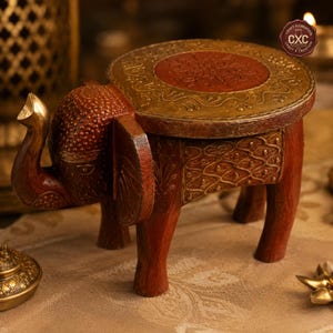 Peut inclure: Une table d'appoint en bois en forme d'éléphant faite à la main. La table a un plateau rond avec une bordure dorée et un motif central rouge. Le corps de l'éléphant est brun rougeâtre avec des accents dorés. La table mesure environ 30 cm de haut.