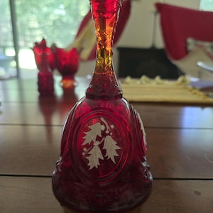 Puede incluir: Una campana de cristal rojo rubí con un mango texturizado y un panel ovalado central decorado con un diseño esmerilado blanco de hojas de acebo y bayas. La campana tiene una base acampanada con patrones florales en relieve en el borde.