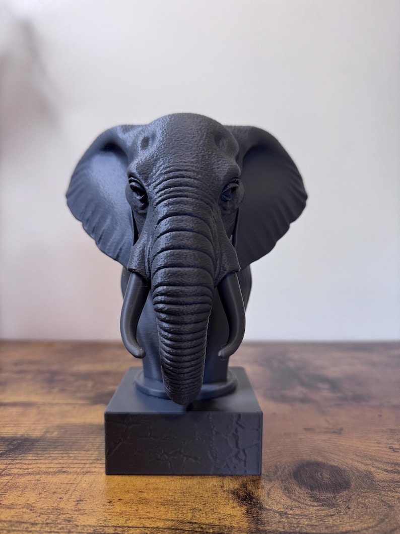 May include: A dark gray elephant bust sculpture with detailed wrinkles and tusks. The elephant is mounted on a square base. The sculpture is a decorative item.