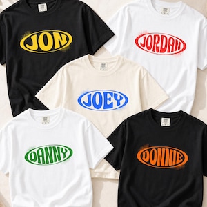 May include: Five short-sleeve crewneck t-shirts in black, white, and cream. Each shirt features a central oval graphic with a name printed in a bold font: JON in yellow, JORDAN in red, JOEY in blue, DANNY in green, and DONNIE in orange.