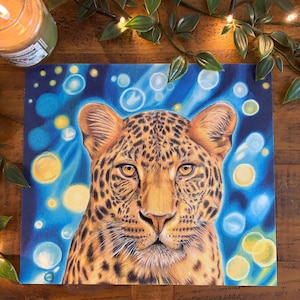Könnte beinhalten: Detaillierte Zeichnung eines Leoparden-Gesichts mit einer warmen Farbpalette aus Braun-, Orange- und Gelbtönen. Das Fell des Leoparden ist mit dunklen Flecken gesprenkelt. Der Hintergrund hat blaue und gelbe Kugeln, die einen verträumten Effekt erzeugen.
