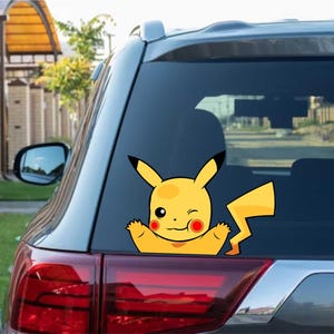 Può includere: Un adesivo giallo di Pikachu con dettagli neri, che fa l'occhiolino e saluta, è applicato sul lunotto posteriore di un veicolo. L'adesivo è un'illustrazione a cartoni animati del famoso personaggio Pokémon.