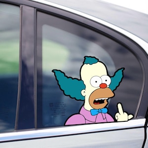 May include: A car window sticker depicting Krusty the Clown from The Simpsons. The cartoon character is shown with his green hair, red nose, and blue bow tie, giving the middle finger. The sticker is applied to a car window.