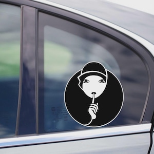 May include: A black and white car decal featuring a stylized illustration of a person with a finger over their lips, in a circle. The person is wearing a hat. The decal is affixed to a car window.