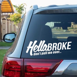 Puede incluir: Adhesivo de vinilo blanco para coche con el texto "Hella BROKE" en una fuente estilizada, y "don't pull me over..." debajo. El adhesivo está en la ventana trasera de un coche plateado.