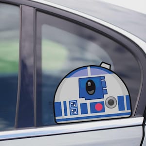 Könnte beinhalten: Ein blauer, weißer und grauer R2-D2 Autoaufkleber ist an einer Autoscheibe angebracht. Der Aufkleber zeigt den Kopf des Droiden mit blauen Paneelen, einem roten Kreis und einem schwarzen Auge. Das Auto ist silberfarben.