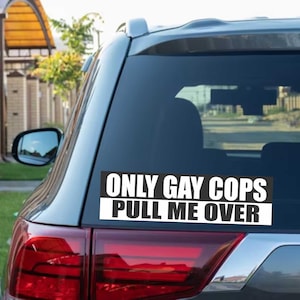 Op de afbeelding: Een rechthoekige bumpersticker op de achterruit van een auto. De sticker heeft zwarte tekst die luidt "ONLY GAY COPS PULL ME OVER" op een witte achtergrond. De auto is zilverkleurig met rode achterlichten.