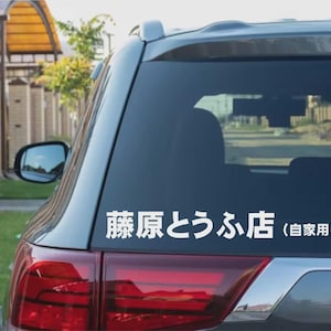 Peut inclure: Autocollant blanc avec texte japonais collé sur la vitre arrière d'une voiture grise. Le texte se lit "藤原とうふ店 (自家用)". La voiture est garée à l'extérieur, avec un cadre résidentiel en arrière-plan.