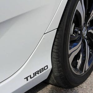 May include: A white car's side panel with a black "TURBO" decal. The image shows a black tyre and a silver and black alloy wheel. The wheel has a Honda logo in the centre.