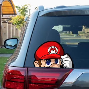 Peut inclure: Autocollant de fenêtre de voiture représentant Mario, le personnage de la franchise Super Mario Bros. Mario porte sa casquette rouge emblématique avec un "M" blanc et regarde par la fenêtre de la voiture.