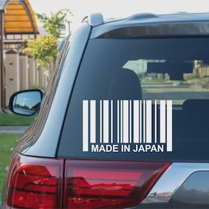 Puede incluir: Calcomanía de vinilo blanco de un código de barras con el texto "MADE IN JAPAN" debajo. La calcomanía está adherida a la ventana trasera de un vehículo gris. El diseño del código de barras se compone de líneas verticales.