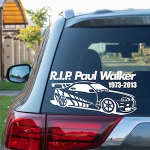 May include: White vinyl car sticker with a sports car design and the text "R.I.P. Paul Walker 1973-2013". The sticker is affixed to the rear window of a car, with the red taillight visible below.