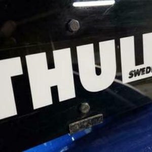 May include: Close-up of a black surface with the white "THULE" logo and the word "SWEDEN" below it. The logo is a bold, sans-serif font. The surface appears to be part of a vehicle accessory.