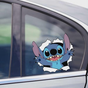 Könnte beinhalten: Ein blauer Stitch-Aufkleber, der die Figur aus dem Zeichentrickfilm zeigt, ist auf einer Autoscheibe angebracht. Stitch ist zu sehen, wie er durch ein zerrissenes Loch bricht, mit einem breiten Grinsen und ausgestreckten Armen. Der Hintergrund ist eine Autotür.