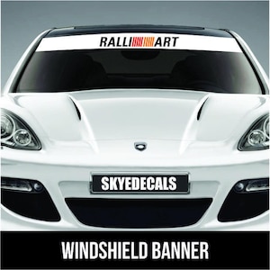May include: White windshield banner with the text "RALLIART" in black and red/orange stripes. The banner is on a white car with the text "SKYEDECALS" on the license plate. The bottom of the image has the text "WINDSHIELD BANNER".