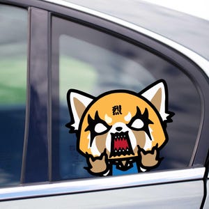 Peut inclure: Un autocollant de fenêtre de voiture représentant un panda roux de dessin animé en colère avec un visage noir et blanc, une fourrure orange et une bouche rouge. L'autocollant porte du texte japonais au-dessus des yeux du panda.