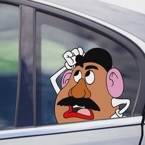 May include: A cartoon decal of Mr. Potato Head with a surprised expression, peeking out from a car window. The decal features a brown face, black mustache, and pink ears. The car is silver.