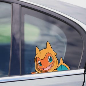 Puede incluir: Una calcomanía para ventana de coche con el personaje Charmander. La calcomanía es naranja con detalles azules y amarillos, y está colocada en una ventana de coche. El personaje está sonriendo.