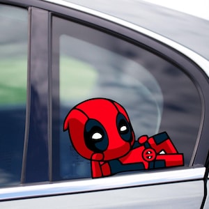 May include: A red and black Deadpool car sticker. The cartoon character is depicted in a relaxed pose, leaning against a car window. A vibrant, eye-catching accessory for any vehicle.
