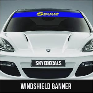 May include: A white car with a blue windshield banner featuring the text "SPOON SPORTS" in yellow. The car also has a license plate that says "SKYEDECALS" and a black banner at the bottom that says "WINDSHIELD BANNER".