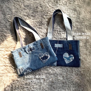 May include: Two denim tote bags with shoulder straps. The left bag is light wash denim with a distressed heart patch and the text LIGHT WASH OPTION 1. The right bag is dark wash denim with a distressed heart patch and the text DARK WASH OPTION 2.