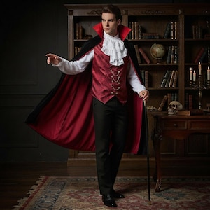 Può includere: Un costume composto da un mantello nero con fodera rossa e colletto alto, un gilet rosso a motivi con catene dorate, una camicia bianca a maniche lunghe con jabot a volant, pantaloni neri e un bastone da passeggio nero con pomello dorato.