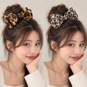 Peut inclure: Deux nœuds pour cheveux avec des motifs imprimés léopard. L'un présente une base brun doré avec des taches noires, tandis que l'autre a une base crème avec des taches brun foncé et noires. Les deux nœuds sont noués dans un style classique.