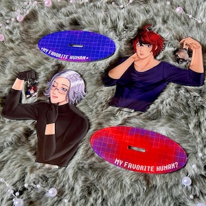 May include: Two acrylic character standees featuring a red-haired figure in a dark blue shirt and a silver-haired figure in a black turtleneck, accompanied by two oval bases with grid patterns and the text MY FAVORITE HUMAN+ and MY FAVORITE HUMAN?