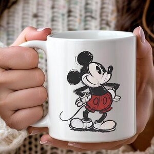 May include: A white ceramic mug with a black handle and the text "But First, Coffee" in a black, handwritten-style font. The mug is on a white surface.