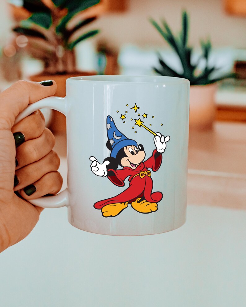 May include: White ceramic mug with a colourful illustration of Mickey Mouse as a wizard. Mickey wears a blue hat with stars, a red robe, and yellow shoes. He holds a wand with stars. The mug has a white handle. The design is from a popular cartoon.