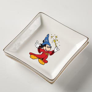 May include: Square white ceramic dish with gold trim featuring a colorful graphic of Mickey Mouse in a wizard costume. Mickey is holding a wand with stars. The dish is likely for decorative use or serving small items.